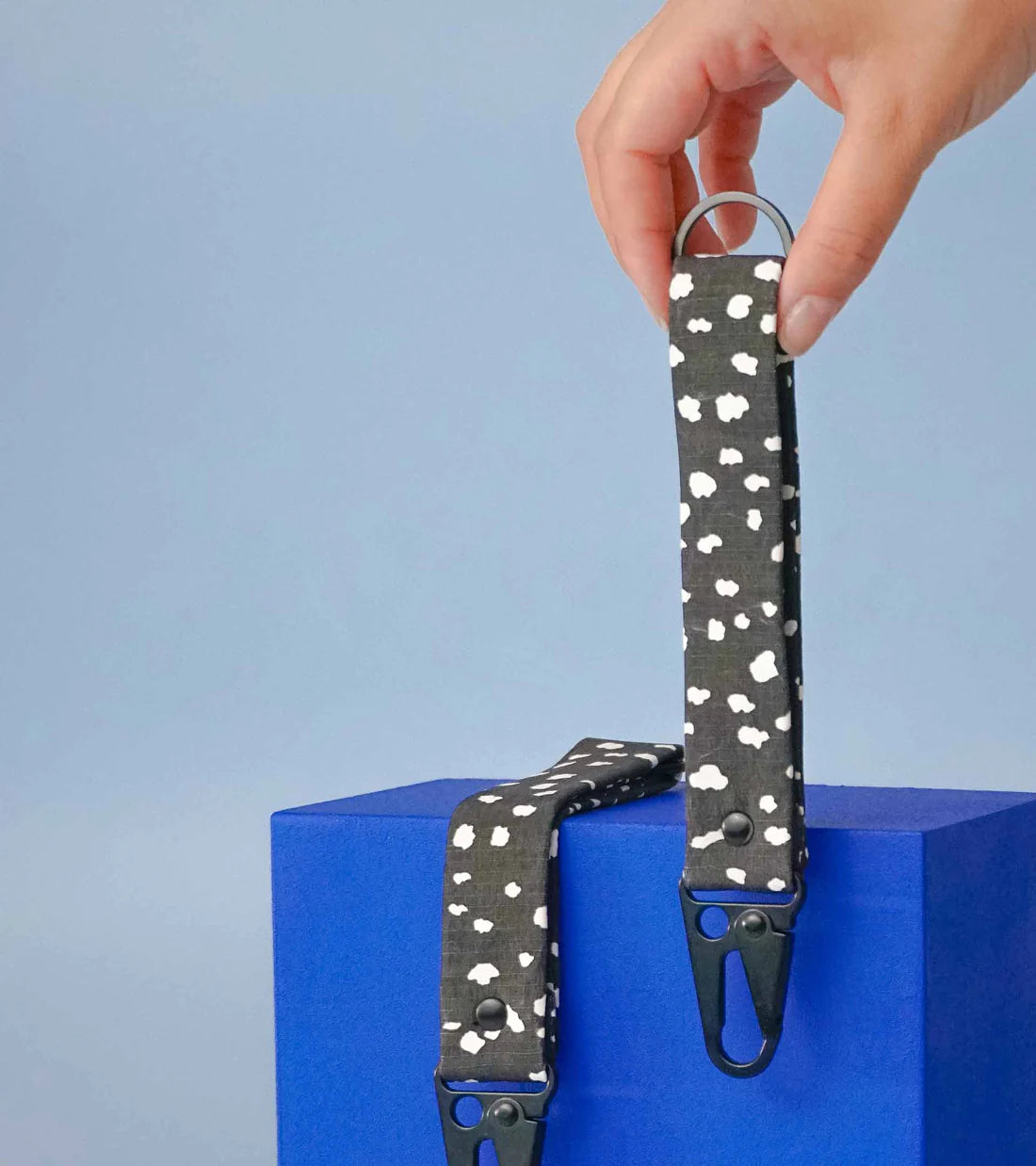 Two Notabag Keychains in black sprinkle pattern, one held by a hand and the other laid across a box