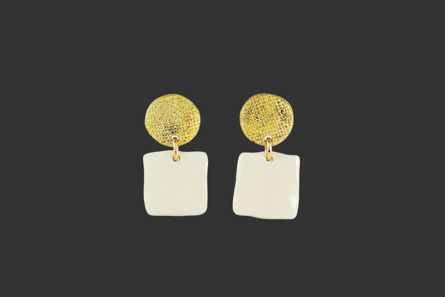 Gold and white earrings on a grayish background