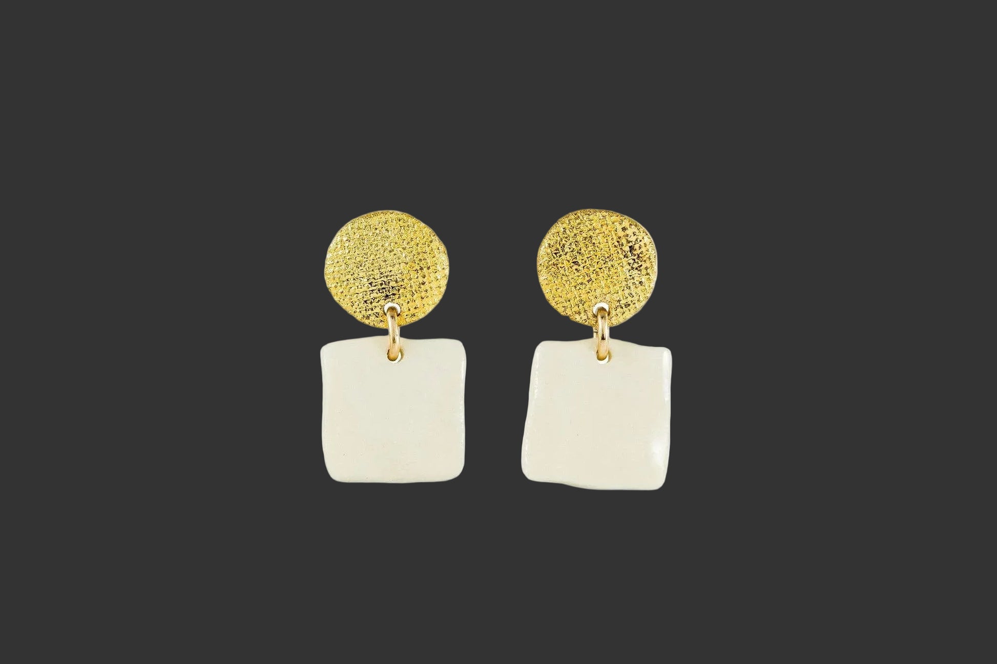 Gold and white earrings on a grayish background