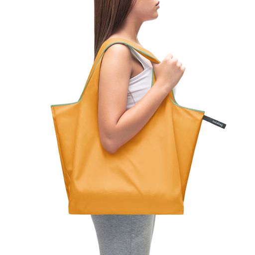 A woman dressed in jeans and a t-shit holds a Notabag tote bag in yellow on her shoulder