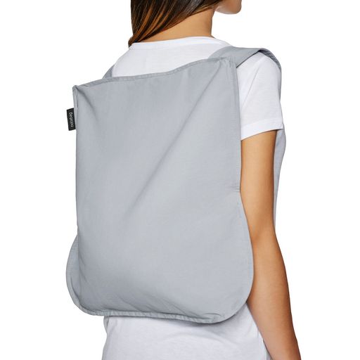 A woman models a grey Notabag, foldable reusable, tote plus backpack her back.